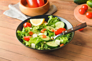 Bowl of delicious salad with vegetables and feta cheese on wooden table