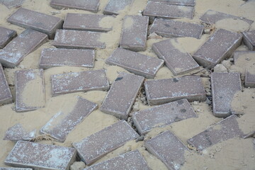 Damaged road with potholes, break in sidewalk, paved with gray blocks. Bad road.