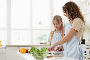Obraz na płótnie Canvas Mother and teen daughter preparing vegetable salad at kitchen