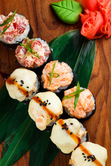 japanese sushi rolls with cheese cap and roll with raw salmon and tuna in a restaurant serving on a wooden board on a dark background. top view.