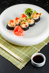 baked salmon sushi rolls on a white plate with wasabi and ginger on a dark background with makisu and bamboo sticks