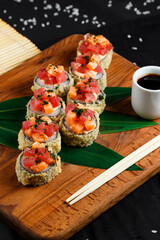 tempura roll with salmon and tuna on a wooden board with red ginger and soy sauce on a dark background close-up