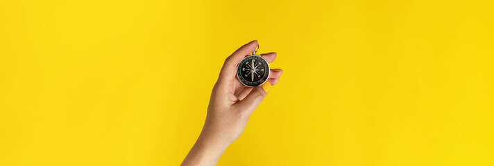 Female hand holding a compass on a yellow background with copy space - obrazy, fototapety, plakaty