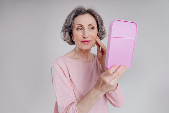 Mature woman looking at mirrow on grey background
