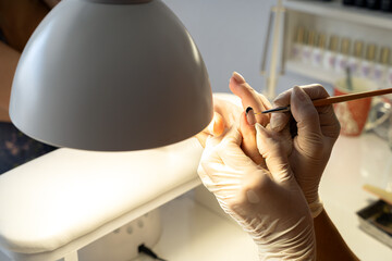 The manicure master applies a decorative coating with a brush to the client's nail. Close-up, fine tool work..