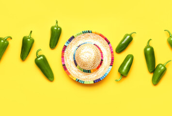 Green jalapeno peppers and sombrero hat on color background