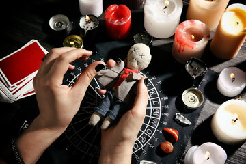 Woman stabbing voodoo doll with needle at table, closeup. Curse ceremony