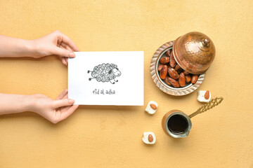 Female hands with greeting card for Eid al-Adha (Feast of the Sacrifice), Turkish sweets and coffee on color background