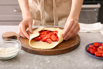 Obraz na płótnie Canvas Woman preparing strawberry galette on table in kitchen