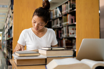 Young Asian women are searching for books and reading books on the tables and aisles of the college...