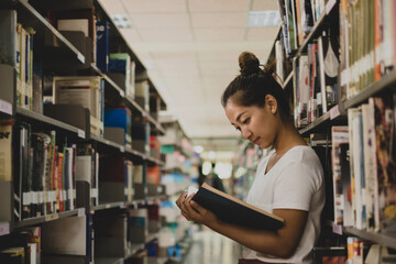 Young Asian women are searching for books and reading books on the tables and aisles of the college libraries to research and develop their academic and education self - Powered by Adobe
