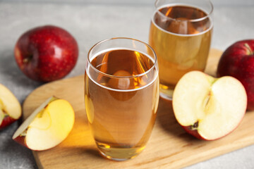 Delicious cider and ripe red apples on grey table