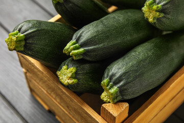 Wooden box with fresh zucchini squashes on dark wooden background, closeup