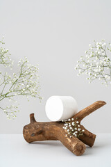 White plastic jar for branding on wooden branch podium and gypsophila flowers on grey background....