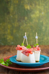 Appetizer, melon with prosciutto on a blue plate on a brown wooden background. Snack recipes.