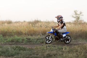 Plakat Child on his small motorcycle. Small biker dressed in a protective suit and helmet. The kid is engaged in motocross.