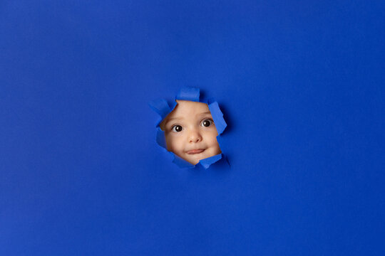 Funny baby face peeking through deep blue paper