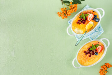 Two creme brulee desserts with fresh strawberries, currants and blueberries on a green stone table.