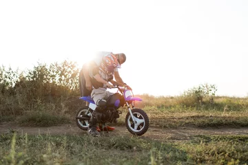 Kid on a motorcycle doing motocross. A little boy learns to ride a motorbike. The coach teaches the child to drive a motorcycle. Son and father on the track. © Aleksandr