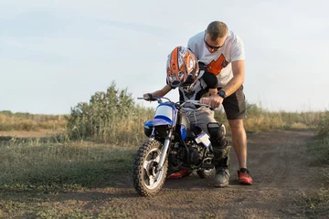Kid on a motorcycle doing motocross. A little boy learns to ride a motorbike. The coach teaches the child to drive a motorcycle. Son and father on the track. © Aleksandr