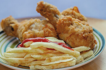 Plate with fries and fried chicken on a wooden table.