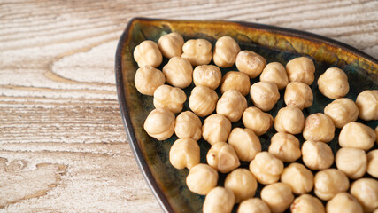 Peeled roasted hazelnuts on a plate. A pile of dried peeled roasted hazelnuts on a white wooden table.