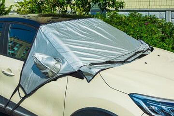 A car in a parking lot with a windscreen covered with a sunscreen reflector on the outside