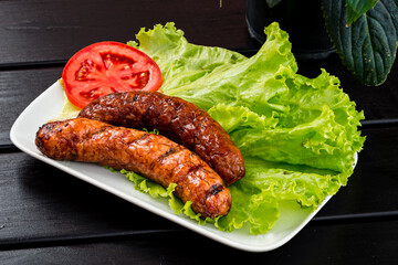 delicious hot grilled bratwurst and fresh vegetables lettuce salad on plate on black wooden table