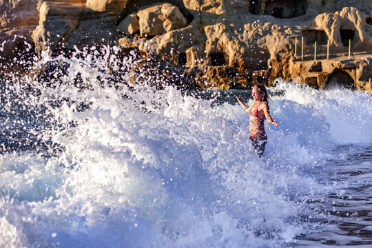 A high wave on the beach of Matala on the island of Crete hits a girl in a bikini
