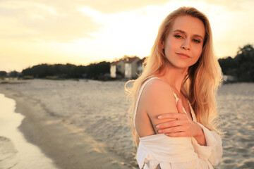 Beautiful young woman on beach at sunset, space for text