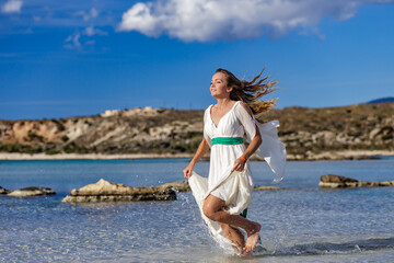 Fototapeta na wymiar Attractive women in white dress running through the water at the Elafonisi beach, Greece. 