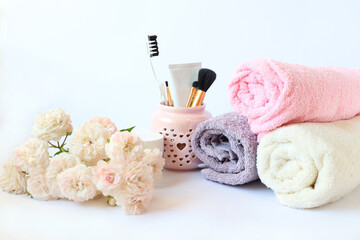 Obraz na płótnie Canvas The concept of morning self-care. Bath towels, toothbrush, paste, makeup brushes in a cup, delicate roses on a light background, a place for text