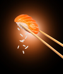 Fresh traditional japanese sushi with salmon between chopsticks on black background