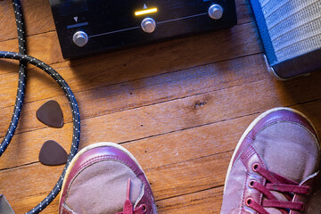 Guitarist's point of view on the stage floor. Guitar pedal, cable, guitar pick, amplifier and shoes...