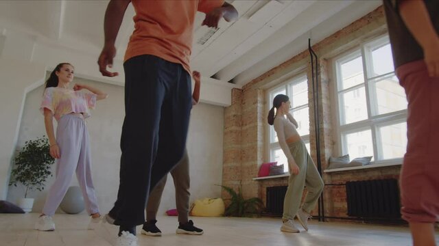 PAN of young multiethnic men and women in sportswear learning moves with female teacher during dance class in studio