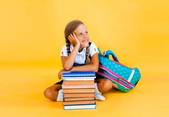 schoolgirl isolated on yellow background with globe. little girl in school uniform sitting on a...