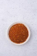 ground dried red chilli, spicy pepper powder on a plate, isolated on white textured background
