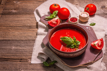 Tomato soup with basil in a bowl. Ripe vegetables, fresh greens, fragrant spices. Vintage wooden table, copy space