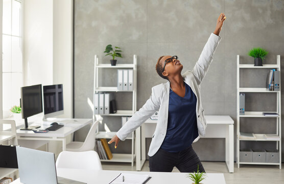Beautiful short haired young black woman has lots of energy for active and productive work day. Happy energetic African American corporate worker or business lady in suit dancing in modern office