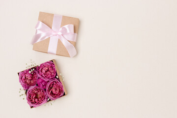Open gift box with rose flowers inside. Present for springtime holidays on a beige background with copyspace.