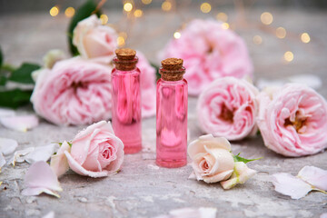 a bottle of rose oil on a background of rose flowers and bokeh