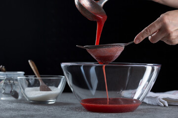 Woman straining strawberry jam through a sieve, home cooking and cooking concept