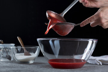 Woman straining strawberry jam through a sieve, home cooking and cooking concept