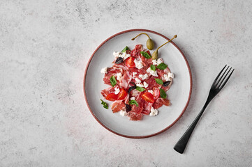 Prosciutto coppa di parma ham slices with ricotta cheese, tomato, capers and basil on light plate with black fork. Top view. Copy space