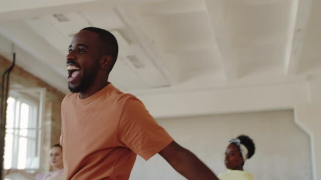 Tilt down shot of happy Afro-American man in sportswear smiling and dancing together with group of diverse students during dance class