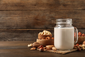 Vegan milk and different nuts on wooden table. Space for text