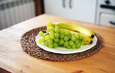 Close up of green grapes and bananas in plate on kitchen table