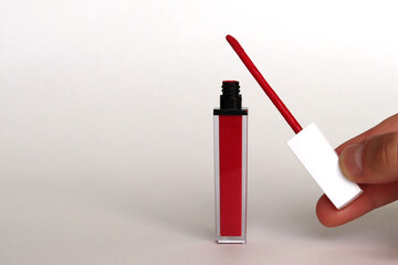 A man's hand holds a brush of lip gloss, next to a jar of red glitter