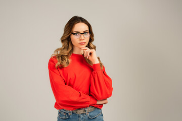 pensive woman in eyeglasses looking at camera isolated on grey