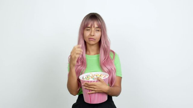 Young woman with pink hair holding a bowl of popcorns and thinking over isolated background